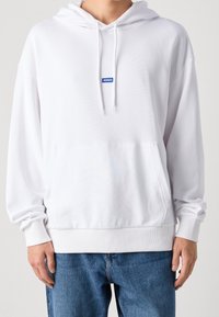 Sudadera blanca con capucha hecha de algodón suave, que presenta un bolsillo tipo canguro, puños de canalé y un pequeño logotipo azul en el pecho.