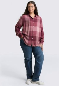 Long-sleeve button-up shirt in a pink and burgundy plaid pattern, paired with blue jeans and white sneakers. The shirt features a relaxed fit.