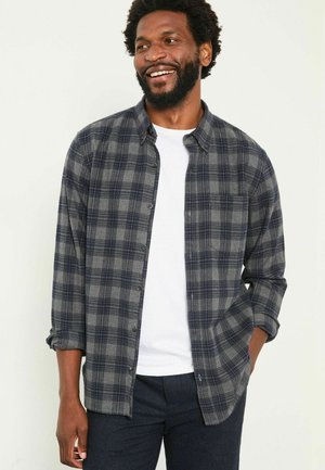 Flannel shirt in dark gray with navy plaid pattern, featuring a button-down collar, chest pocket, and rolled-up sleeves. White T-shirt underneath.