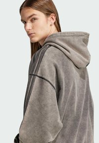 Hoodie i en bleknad grå färg, med en avslappnad passform, textilstruktur och tre vertikala ränder på axeln.