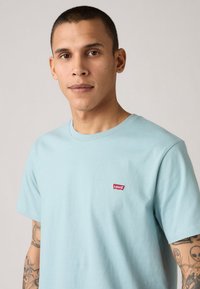 Tricou din bumbac de culoare albastră deschisă, cu guler rotund și un mic logo roșu Levi's pe piept. Mâneci scurte și o croială lejeră.