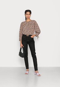 Blusa floral de mangas longas, calças pretas de cintura alta, mules de bloco lilás e uma bolsa preta de vime. Conjunto casual.