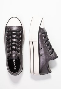 Svarta lädersneakers med en klassisk design, vit gummitå, svarta snörning och en strukturerad yta. Har en logotyp p å tungan.