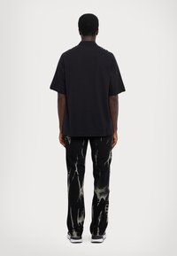 Čierna košeľa s krátkym rukávom a golierom, doplnená o čierne nohavice so vzorom bieleho tie-dye. Celý vzhľad dopĺňajú tenisky s gumovou podrážkou.