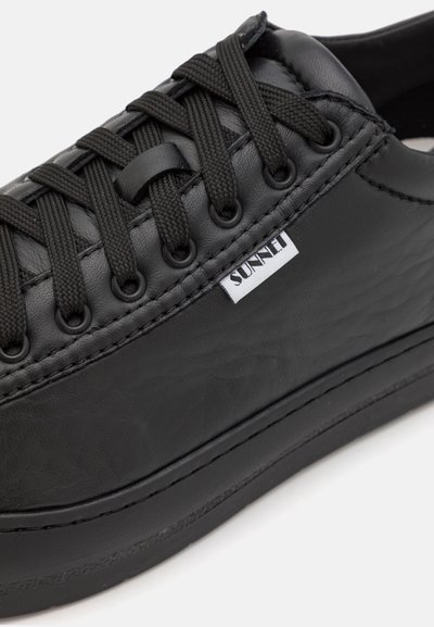 Sneaker din piele neagră cu finisaj texturat, șireturi plate negre și detalii cusute. Prezintă un mic eticheta albă cu logo-ul "SUNSET".