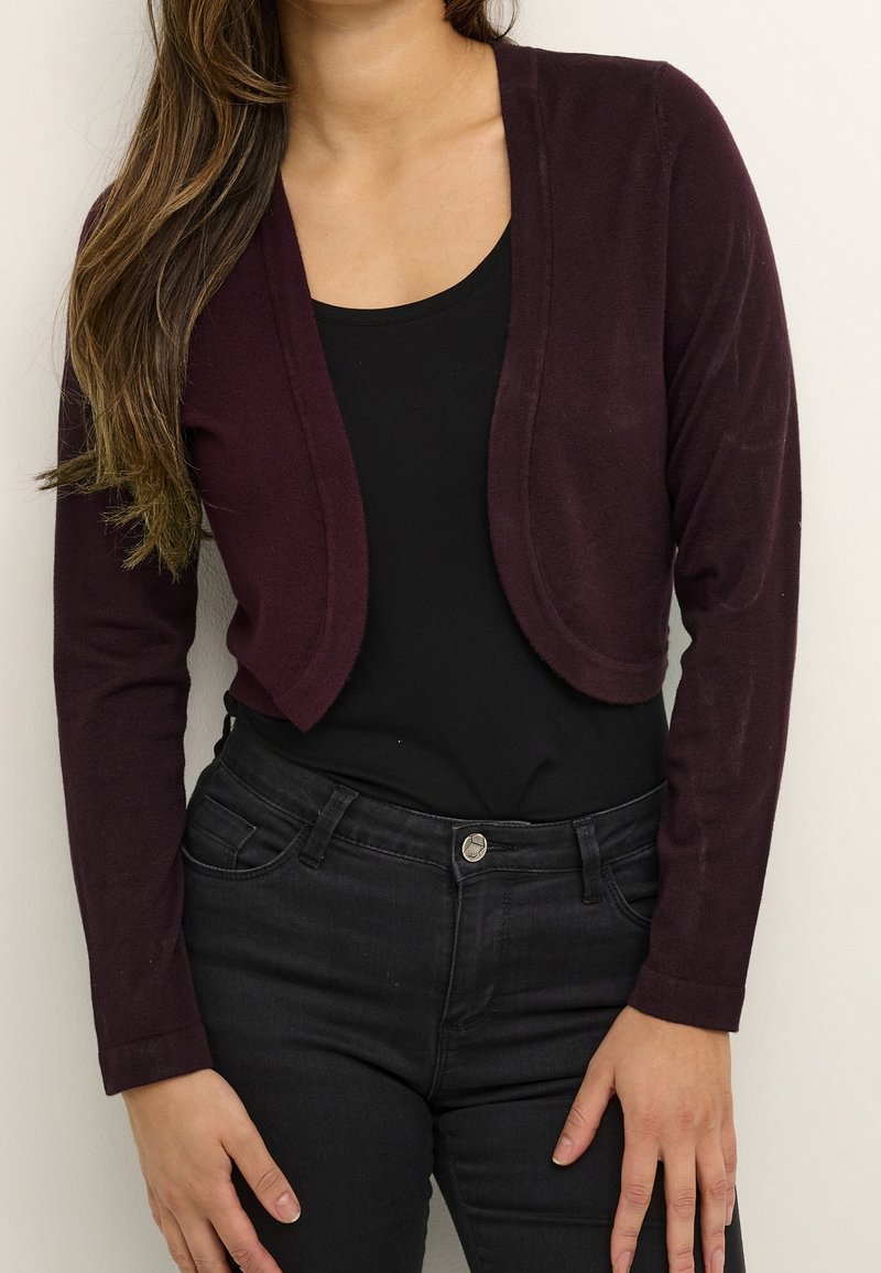 Cardigan bordeaux court à manches longues, texture lisse, design à ouverture frontale, assorti à un haut noir et un jean noir.