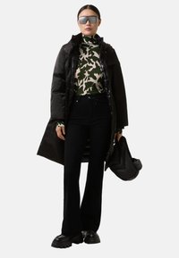 Černý dlouhý péřový kabát, zelený a krémový vzorovaný rolák, černé rozšířené kalhoty, masivní černé boty, oversize šedé sluneční brýle, černá taška.