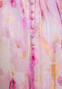 Tessuto rosa pallido con un motivo floreale ad acquerello in tonalità di viola, giallo e arancione, caratterizzato da una fila verticale di piccoli bottoni rivestiti in tessuto.