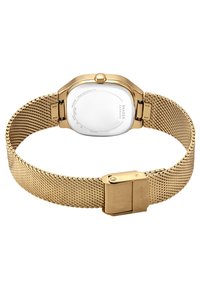 Gold-toned mesh strap wristwatch with clasp, showing the polished stainless steel back engraved with brand and model details.