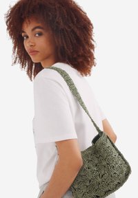 Borsa a spalla verde intrecciata con un motivo testurizzato e una tracolla intrecciata. La borsa ha una forma morbida e sformata, adatta per un uso informale.