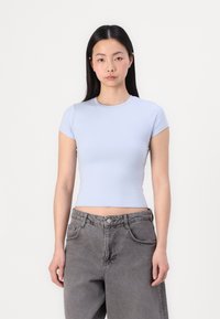 Top curto de manga curta azul claro, feito de tecido elástico, com decote redondo. Combinado com jeans de ganga cinza desbotados de cintura alta.
