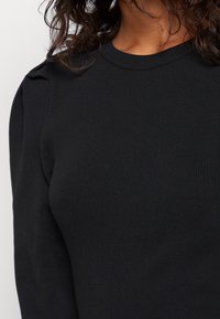 Top de punto acanalado negro de manga larga con detalles de hombros abullonados y escote redondo, textura suave y silueta ajustada.