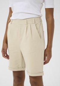 Beige op maat gemaakte shorts met plooien, zijzakken en opgerolde boorden. Gemaakt van een gladde stof, hebben ze een gestructureerde pasvorm en een minimalistisch ontwerp.