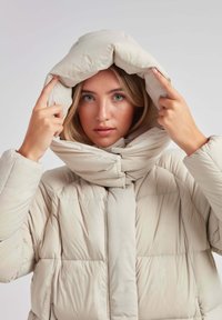 Pufferjakke i lys beige, med en høj, justerbar krave og diagonalt quiltet mønster. Glat stof med en blank finish.