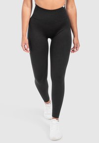Hoge zwarte leggings van rekbaar materiaal, met een gladde textuur en een nauwsluitende pasvorm. Gemaakt in combinatie met witte sneakers.