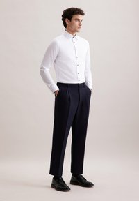 Witte blouse met lange mouwen, een button-down kraag en zwarte knopen, gecombineerd met marineblauwe geplooide broeken en zwarte veterschoenen.