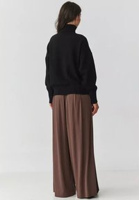 Czarny dzianinowy sweter z wysokim kołnierzem, zestawiony z szerokimi brązowymi spodniami. Outfit charakteryzuje się miękkimi fakturami i luźnymi krojami.