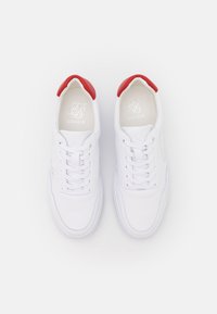 Sneaker bianche con tomaia in pelle liscia, dettagli rossi sul tallone e lacci bianchi. Presenta il logo impresso sulla linguetta. Design classico a bassa punta.