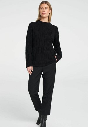 Black cable-knit sweater with long sleeves, round neckline, and textured pattern, paired with black trousers and ankle boots.