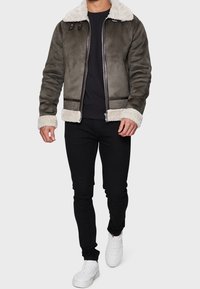 Veste marron doublée en shearling avec accents en cuir noir, fermeture éclair et design ajusté. Associée à un pantalon noir et des baskets blanches.