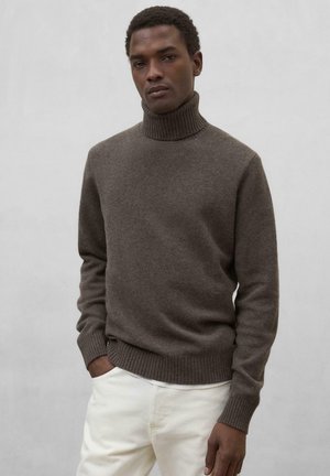 Suéter de cuello alto marrón con textura acanalada y dobladillo, hecho de un material suave. Llevado con pantalones de color claro, diseño minimalista.