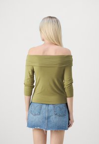 Olivengrønn av- skulder topp med trekvart ermer, kombinert med en lys blå denim miniskjørt med fransede kanter og baklommer.