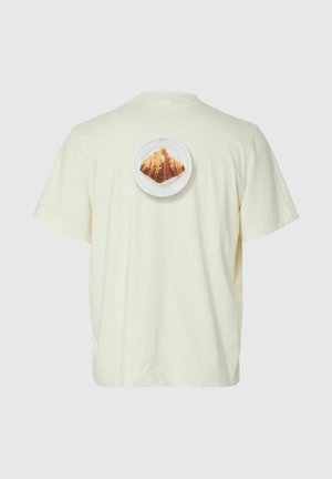 Off-white T-skjorte med en liten tallerken-grafikk med en croissant plassert sentralt på øvre del av ryggen.