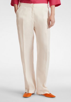 Beige Leinenhose mit geradem Schnitt, ausgestattet mit Fronttaschen, einem Knopfverschluss und einer glatten Textur. Die Schuhe sind leuchtend orange Ballerinas.