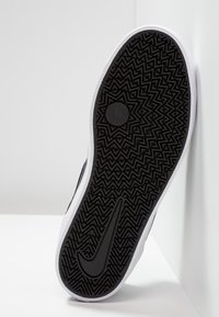 Svart gummisula till sneakers med zigzag-mönster, med en vit kant och en central cirkulär greppdetalj. Nike-logotyp synlig.