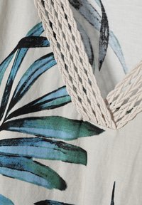 Tessuto a fantasia floreale con foglie blu e verdi su uno sfondo beige, con un dettaglio decorativo di corda attorcigliata lungo il colletto.