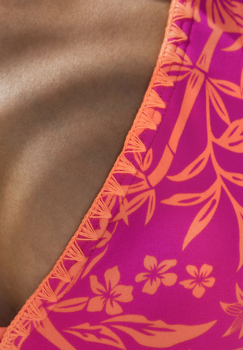 Rosa Bikini-Oberteil mit orangefarbenen Blumenmustern, strukturierten Nahtdetails und einem glatten, kontrastierenden hautfarbenen Stoff auf einer Seite.
