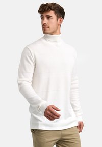 Hvit rullkragesweater med teksturerte striper, ribbede mansjetter og en avslappet passform. Stoffet ser mykt og varmt ut.