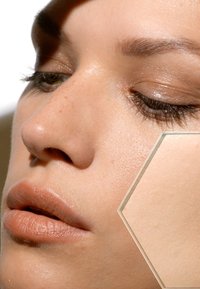 Gros plan d'un visage avec une peau lisse et claire, de légères taches de rousseur et une couleur de lèvres neutre. Un zoom hexagonal révèle les détails de la texture de la peau.