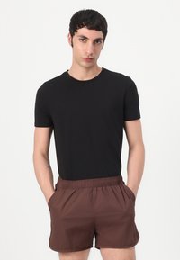 Svart kortermet t-skjorte med rund hals, kombinert med brune svømmebukser med elastisk midje. Begge har en glatt tekstur og et enkelt design.