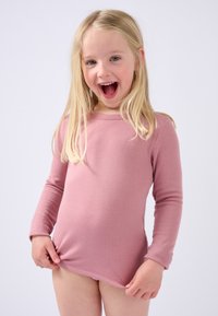 Maglietta a maniche lunghe in morbido cotone rosa chiaro con scollatura a girocollo, caratterizzata da un design aderente e una superficie liscia, indossata da un bambino che tiene il fondo.