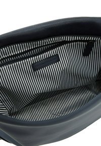 Interno di una borsa in ecopelle nera con fodera a righe bianche e nere. Include una tasca con zip e un'etichetta di marca all'interno.