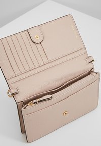 Portefeuille en cuir rose clair avec une fermeture à pression, plusieurs fentes pour cartes et un compartiment zippé pour les pièces. Présente des accents en métal doré.