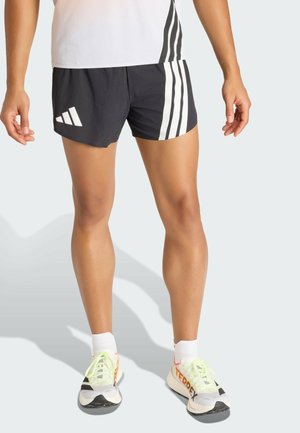 Shorts de sport noirs à rayures verticales blanches, tissu léger, avec un logo distinct sur le côté gauche ; associés à des chaussures sportives.