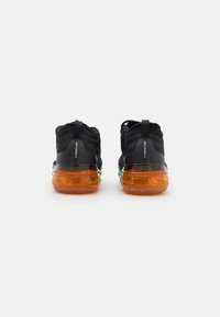 Black textile sneakers with a flexible upper, featuring a transparent orange sole accented by green, and pull tabs at the heel.