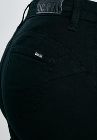 Uzņēmuma "BIG STAR" melnās etiķetes tuvplāns uz melnajām džinsu aizmugurējās kabatas un jostasvietas.