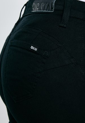 Zbliżenie na tylną kieszeń czarnych dżinsów z denimu z czarną metką marki "BIG STAR" na kieszeni i pasku spodni.