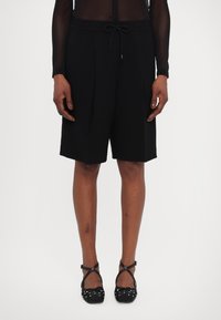 Černé šortky na míru s šňůrkovým pasem, plisovaným předním dílem a bočními kapsami, doplněné balerínami s puntíky. Hladká textura látky.