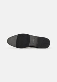 Semelle d'une chaussure habillée noire et grise avec des sections en caoutchouc texturé offrant une bonne adhérence et le nom de la marque "bugatti" embossé près du talon.