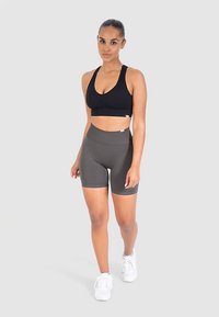 Schwarzer Sport-BH und olivgrüne, hoch taillierte Shorts aus dehnbarem Stoff, mit glatter Textur und enger Passform. Weiße Sportschuhe.