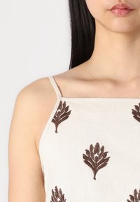 Krémszínű ujjatlan felső vékony pántokkal, barna levélmintás hímzéssel az egész területen, texturált anyagon.