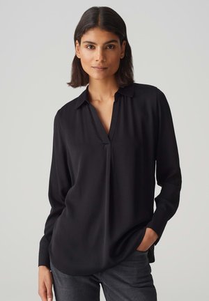 Zwarte lange mouw shirt met een V-hals kraag, gemaakt van gladde stof. Heeft een comfortabele pasvorm en een subtiele drape. Gedragen met donkere jeans.