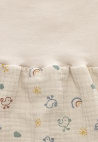 Cotton garment with a beige top and a patterned hem featuring birds, suns, clouds, and rainbows in soft colors on textured fabric.