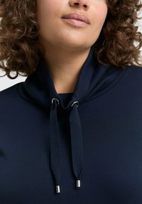 Marineblauwe hoodie met een cowl-neck, voorzien van trekkoorden met metalen uiteinden, gemaakt van zachte stof. Glad textuur met minimale naden.