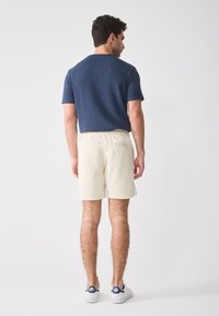 Camicetta corta a maniche corte blu con texture abbinata a pantaloni corti a vita elastica color crema e sneakers bianchi. Design semplice, tessuto dall'aspetto morbido, vestibilità casual.
