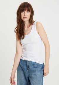 Biała bawełniana koszulka na ramiączkach o dopasowanym kroju i okrągłym dekolcie, w połączeniu z dżinsami typu high-waisted w kolorze niebieskim. Miękka tekstura i casualowy styl.
